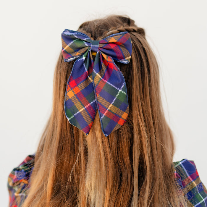girl wearing oversized double fabric bow in navy plaid print with matching twirl dress for back to school