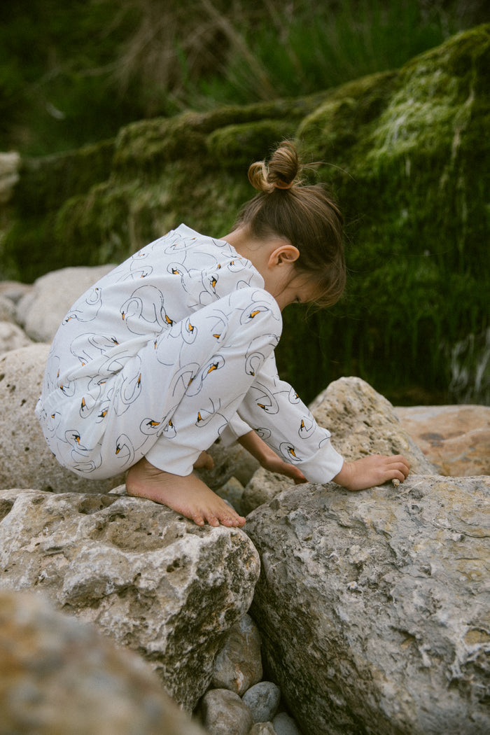 Girl playing on the rocks wearing white cotton Sleepy Doe pyjamas with playful and stylish swan print
