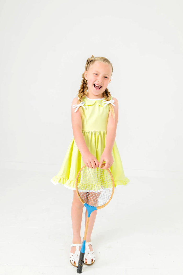 little girl with sports racket in lime green sleeveless twirl dress and white knit pigtail bows