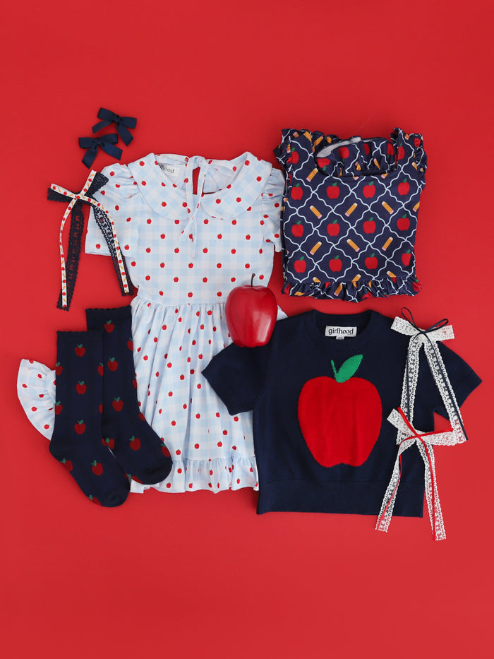 flat lay of coordinating red, blue and white apple themed dresses, sweaters, socks and bows for back to school