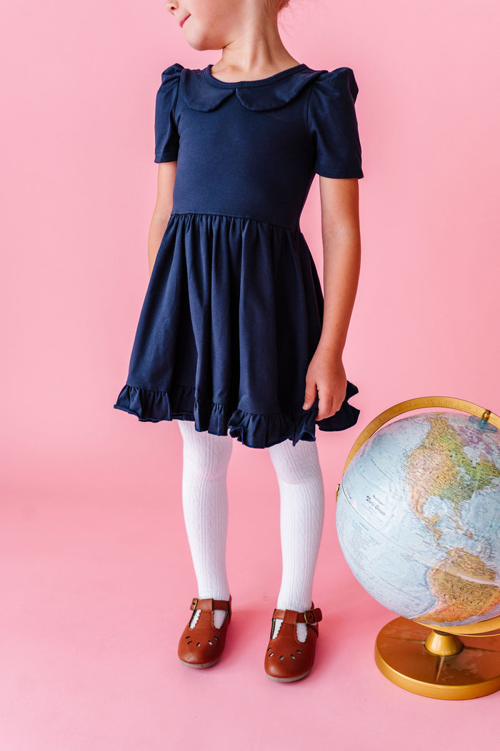 girl wearing navy cotton dress with collar and white cable knit tights