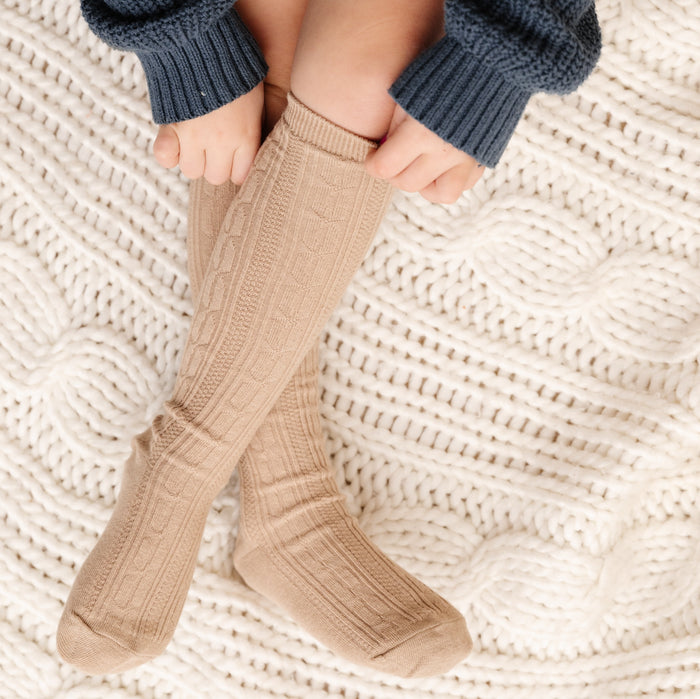 girl pulling up oat brown cable knit socks