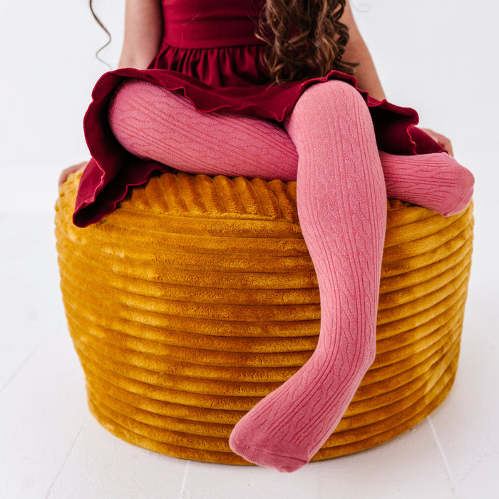 young girl sitting on yellow velvet cushion in pink cable knit tights paired with burgundy twirl dress for fall