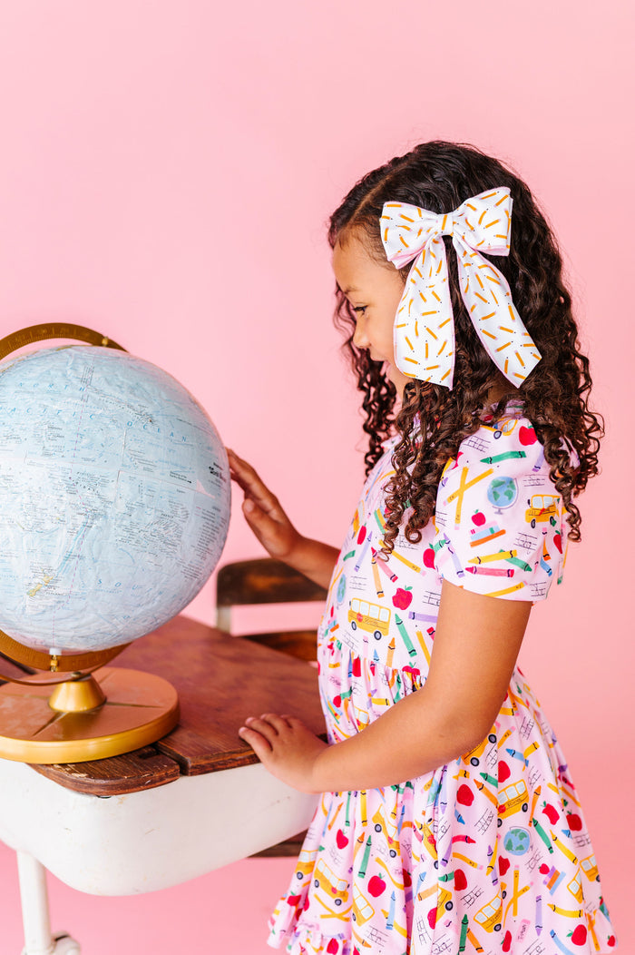 little girl looking at globe wearing back to school outfit with pencil hair bow and pink school print dress