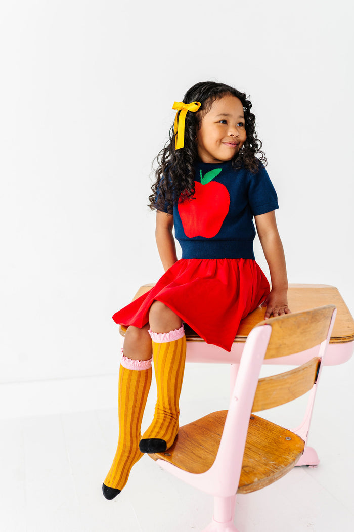 girl wearing colorful back to school outfit with big apple sweater and pencil knee high socks