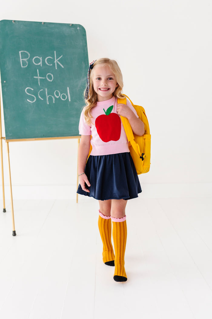 girl wearing 1st day of school outfit, big apple top, navy skort and pencil knee highs