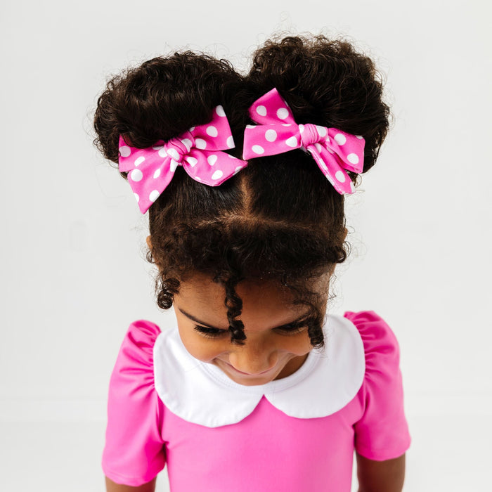 little girl wearing pink fabric bows with white polka dot print to match pink minnie inspired twirl dress