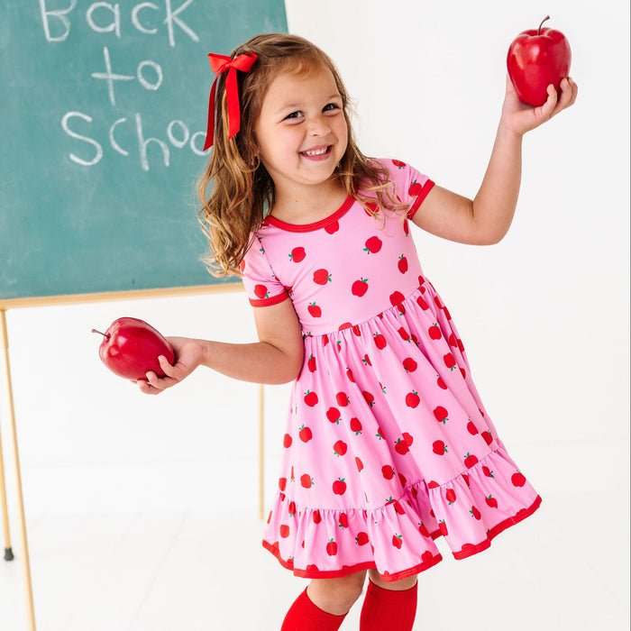 Girl wearing pink and red apples dress and holding apples in back to school scene
