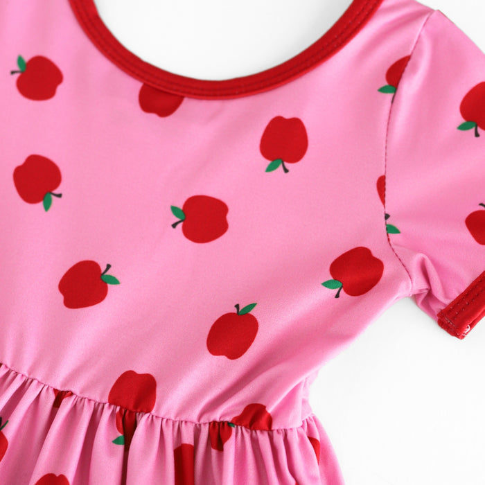closeup of red apple print on pink twirl dress bodice with red trim at the neck and sleeve