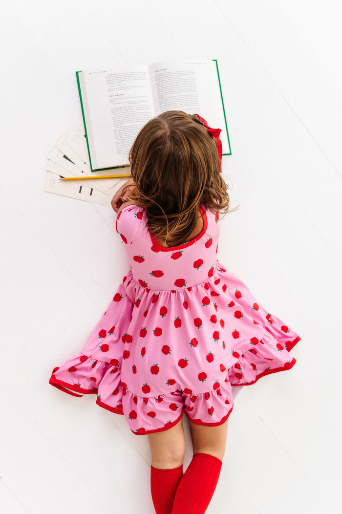 Little girl in pink and red apples dress reading a book