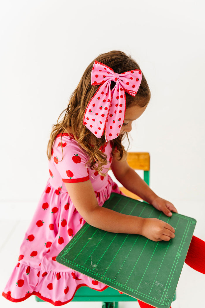 Girl wearing matching pink and red apples hair bow and dress for back to school