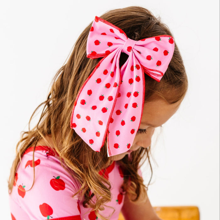 little girl at desk in pink apple print double hair bow on clip paired with matching pink apple print charm dress for school days