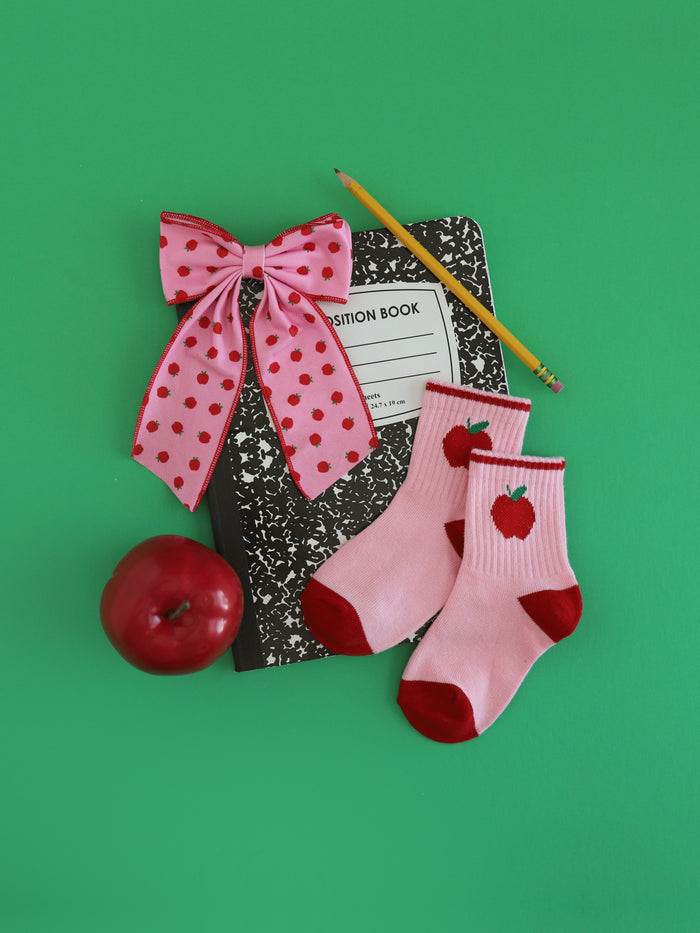 girls' pink apple print haor bow and matching pink crew socks with apple design sitting with school supplies