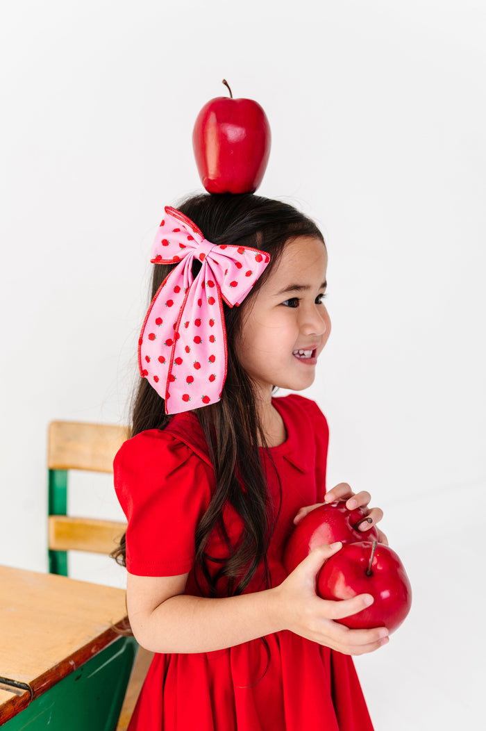 little girl holding apples with apple on her head wearing pink apple print double hair bow paired with bright red twirl dress for school