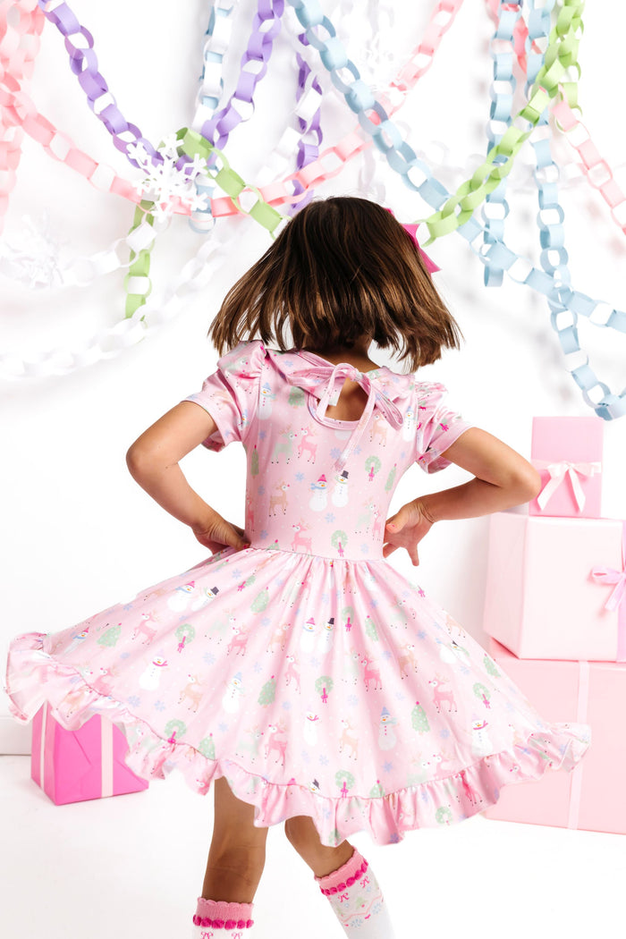 girl twirling in front of winter wonderland decor in pastel pink twirl dress with winter themed Christmas print