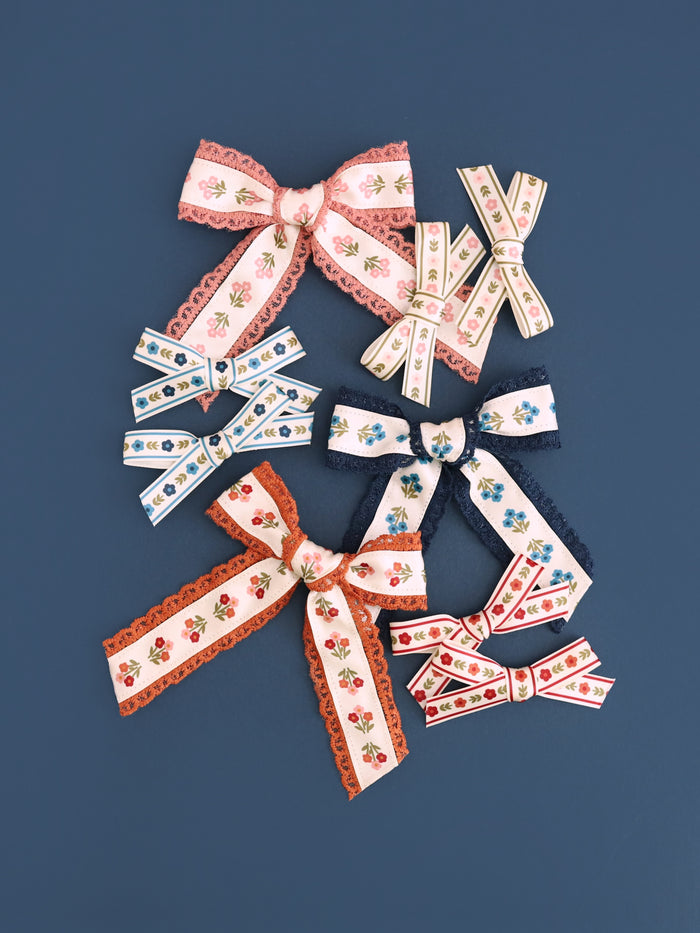 flat lay of girls' posey print lace trimmed and pigtail bows on clips to match fall collection