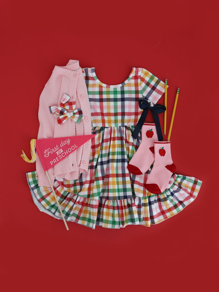girls' primary gingham short sleeve twirly dress styled with light pink knit cardigan, pink apple crew socks, gingham pigtail bows and navy satin bow
