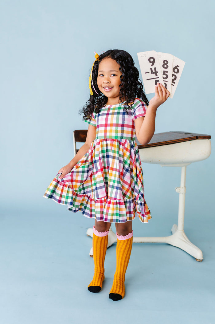 girl holding math flash cards in white with primary color gingham print twirl dress paired with pencil socks and matching lace ribbon bow
