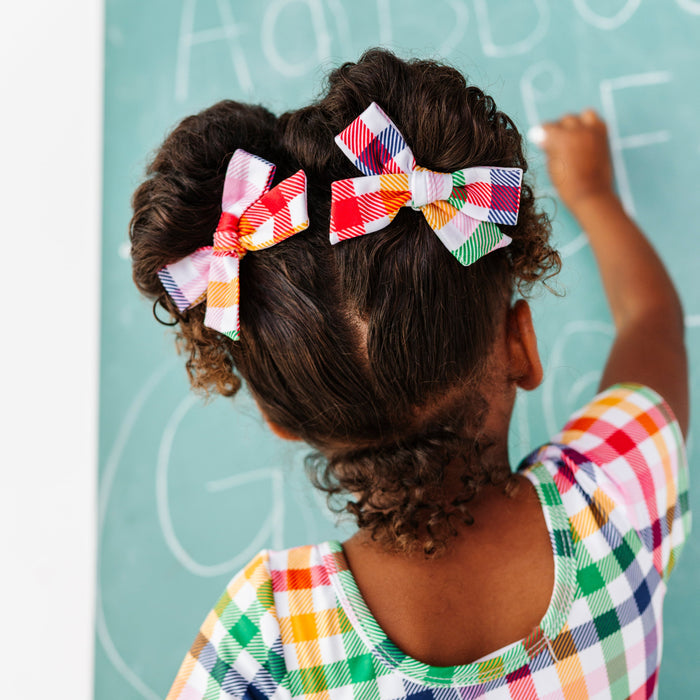 girl drawing on chalkboard in primary gingham print pigtail bows paired with matching print dress for school