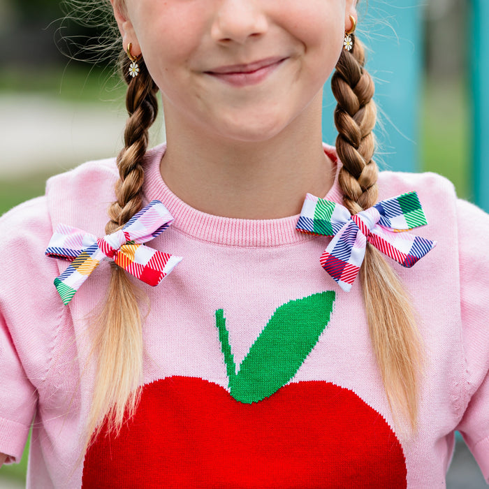 girl in braids with primary gingham print pigtail bows on clips paired with pink apple sweater