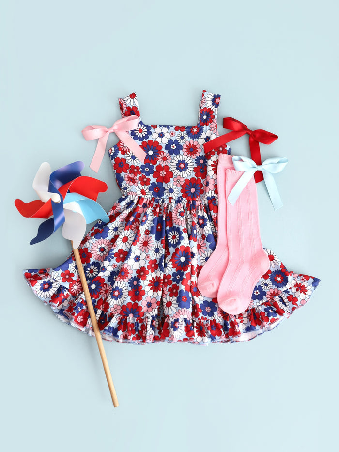 flatlay of girls floral 4th of july summer twirl dress with matching pink scallop knee highs and satin hairbows
