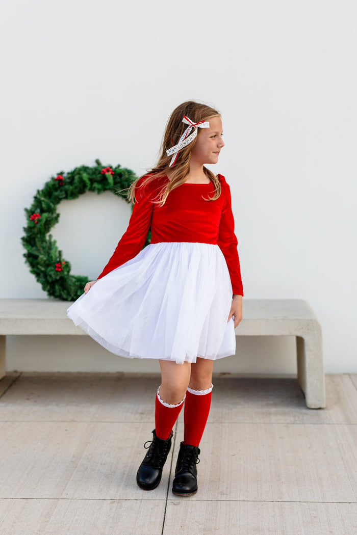 girl in Santa inspired velvet tutu dress with bright red velvet bodice and white tulle skirt paired with red and white knee highs and hair bow