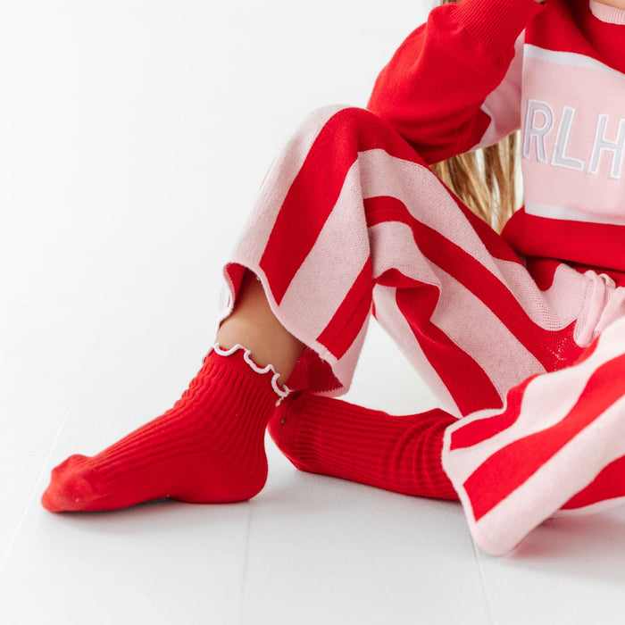 little girl sitting in red and pink girlhoods sweater set with matching red ribbed midi socks with white trim