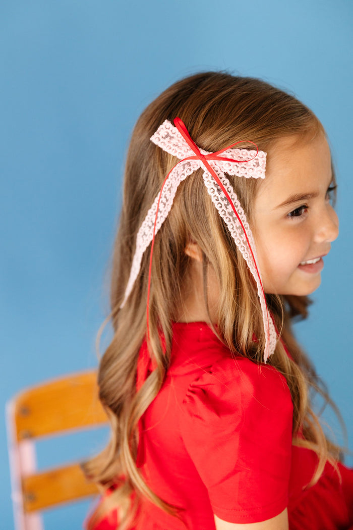 little girl in pink long tail lace bow with skinny red ribbon paired with matching bright red twirl dress for school