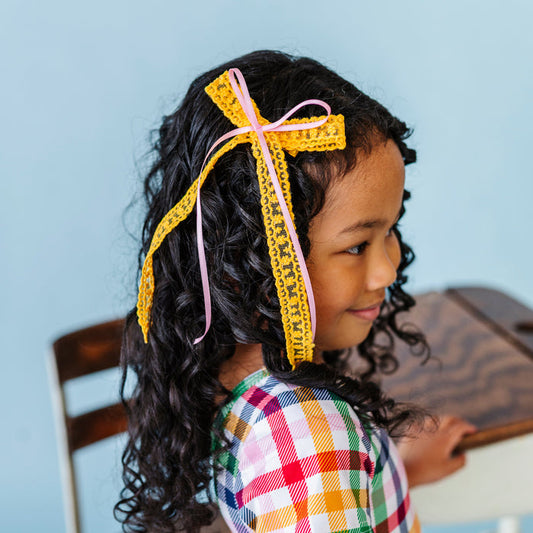 girl in yellow lace long tail bow with light pink satin ribbon for pencil inspired color palette paired with primary gingham twirl dress for back to school