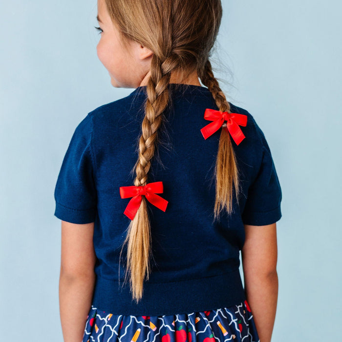 girl in braided pigtails with red satin bows