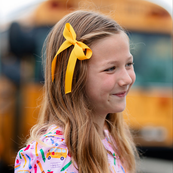girl in front of yellow school bus in pink school themed twirl dress and bright yellow satin hair bow on clip