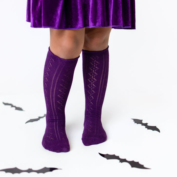 Person wearing a purple skirt and matching knee-high socks with decorative patterns on a white background.