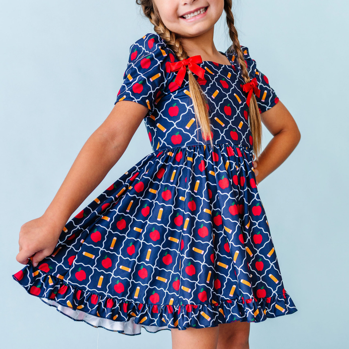 girl wearing navy back to school twirl dress with apple and pencil print and matching red hair bows
