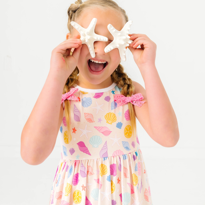 young girl holding starfish wearing sleeveless twirl dress with pastel seashell print