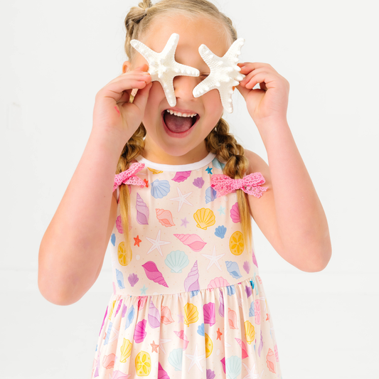 young girl holding starfish wearing sleeveless twirl dress with pastel seashell print