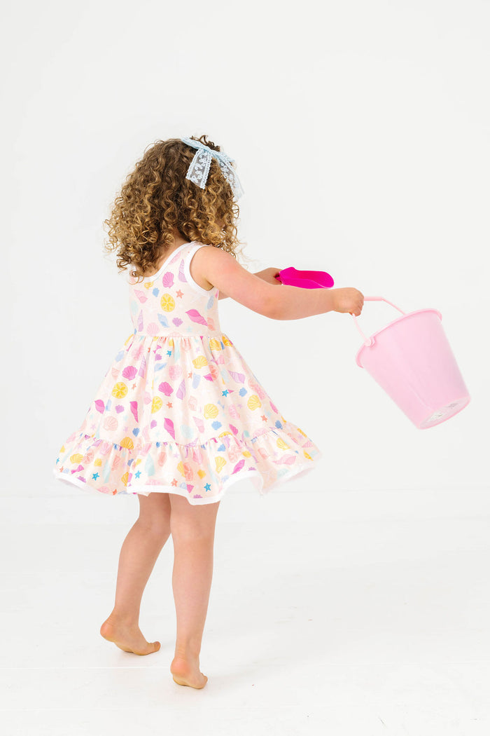 little girl twirling with beach bucket in seashell print sleeveless twirl dress