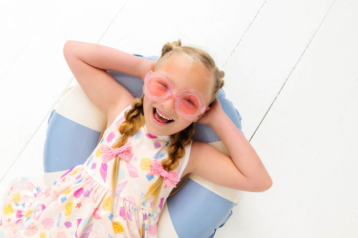 little girl lounging on pool float in seashell print twirl dress and pink lace pigtail bows