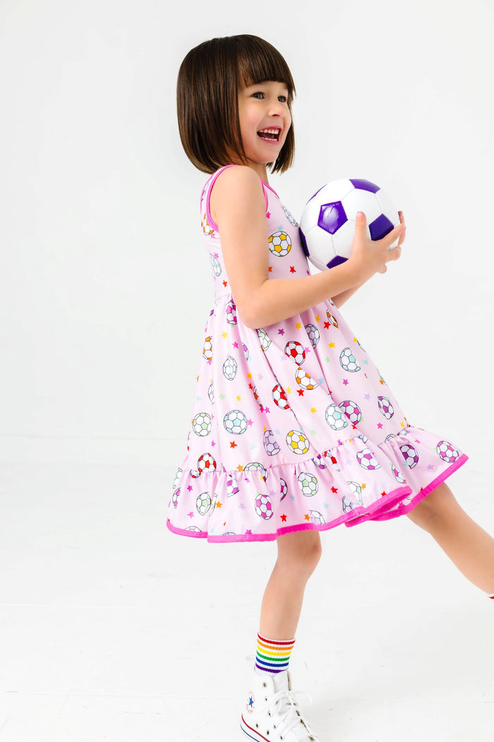 little girl holding soccer ball in colorful soccer ball print twirl dress on pink with rainbow striped crew socks