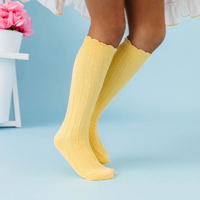 little girl twirling by flowerpots in pastel yellow scallop trimmed knee socks paired with matching striped dress