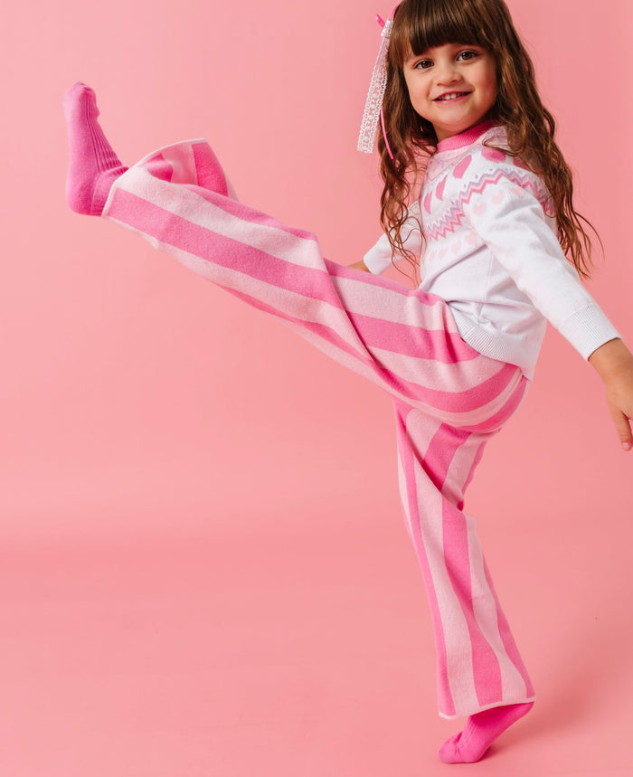 little girl high kicking in two-tone pink striped sweater pants, pink socks and white fair isle sweater with a valentine's theme