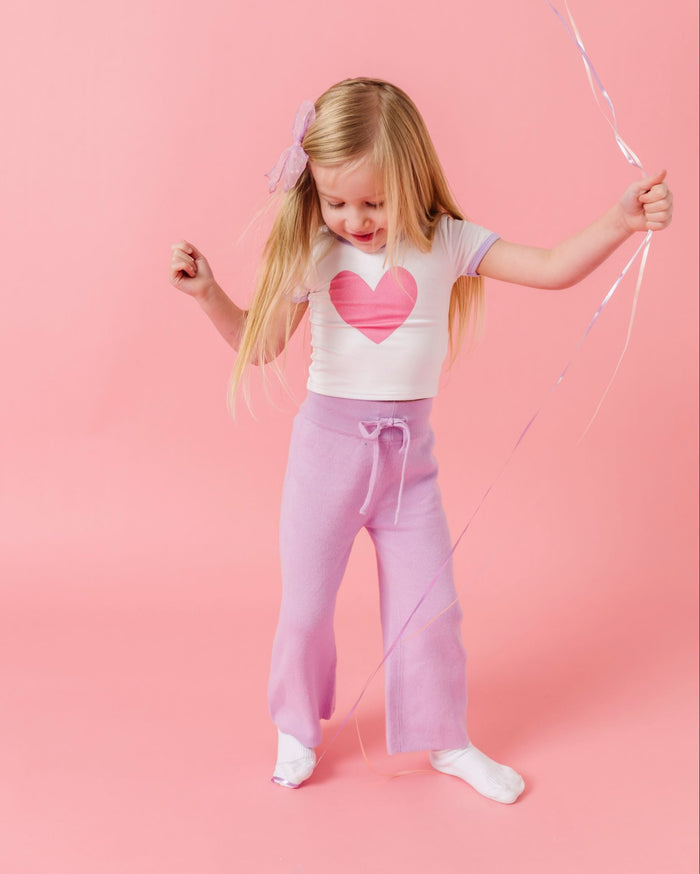 little girl holding balloons in white with pink heart valentines top, lavender knit sweater pants and white socks