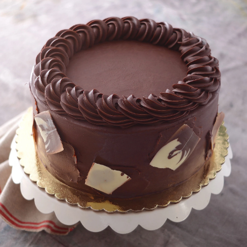 Round cake with dark chocolate frosting, thick piped border, dark and white chocolate shards, on gold board.