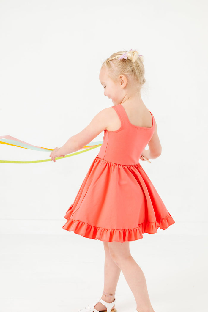 young girl twirling with streamers in coral pink sleeveless twirl dress for summer