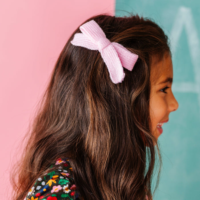 girl wearing light pink yarn knit hair bow on clip with forest green apple and floral twirl dress