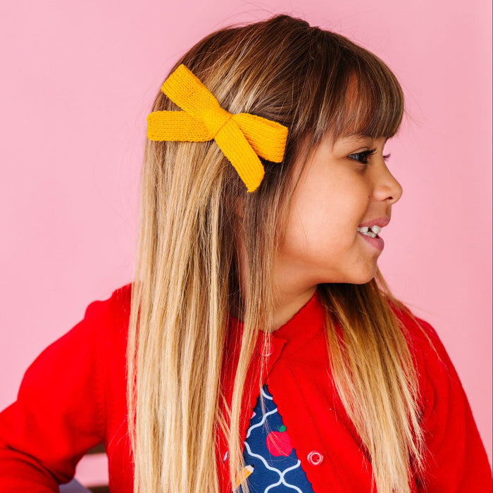 girl wearing yellow yarn knit hair bow with back to school dress and red cardigan
